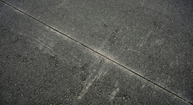 Clean straight saw cut line through dark asphalt pavement — professional asphalt cutting service in Oregon by Neill Sealcoating