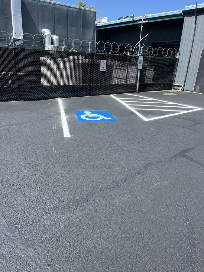 Repainted ADA-accessible parking stall with blue wheelchair symbol and white hatched access aisle on a freshly sealcoated lot on Market Street in Medford, Oregon