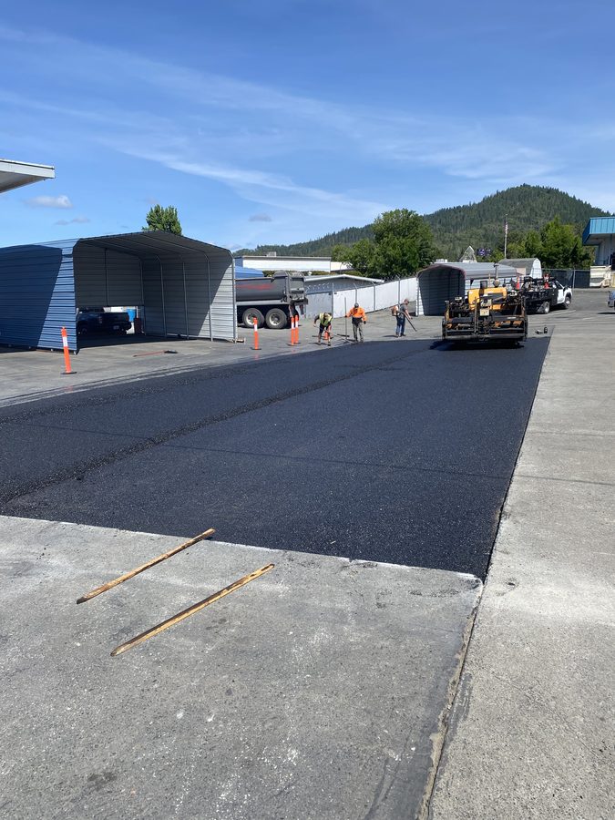 Asphalt paving crew finishing the freshly laid Caveman Towing lot in Grants Pass, Oregon