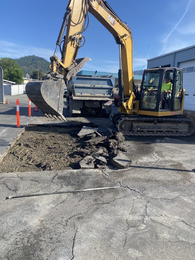 Excavator removing failed asphalt at Caveman Towing to prep for repaving in Grants Pass, Oregon