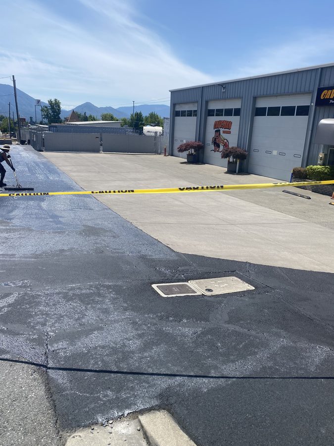 Freshly sealcoated commercial parking lot in front of the Caveman Towing building at 2100 NW Vine St in Grants Pass, Oregon