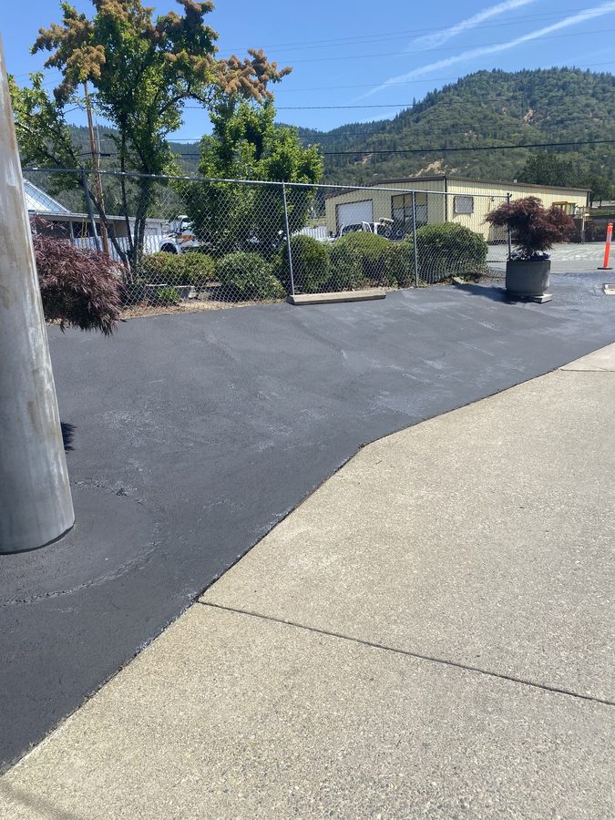 Sealcoated commercial drive aisle along a landscaped fence line at Caveman Towing in Grants Pass, Oregon