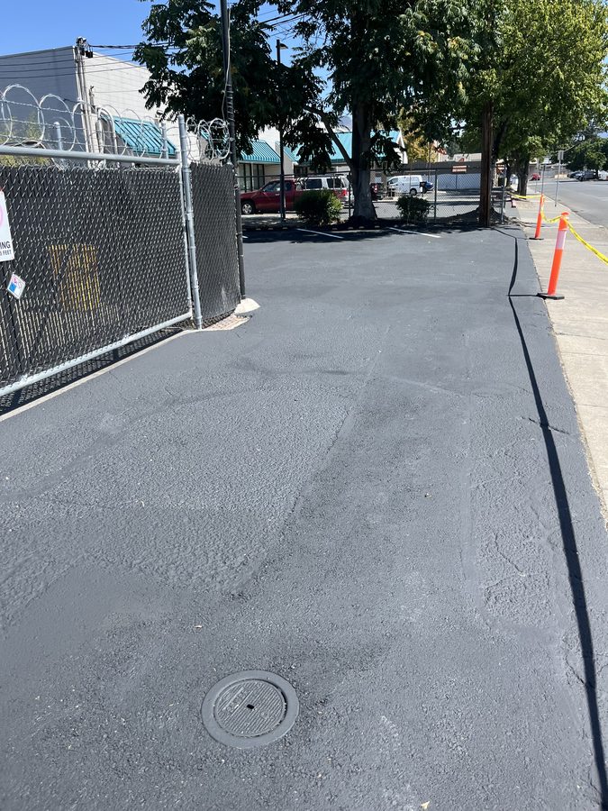 Commercial parking lot sealcoated to a uniform dark finish along the fence line after crack filling on Market Street in Medford, Oregon