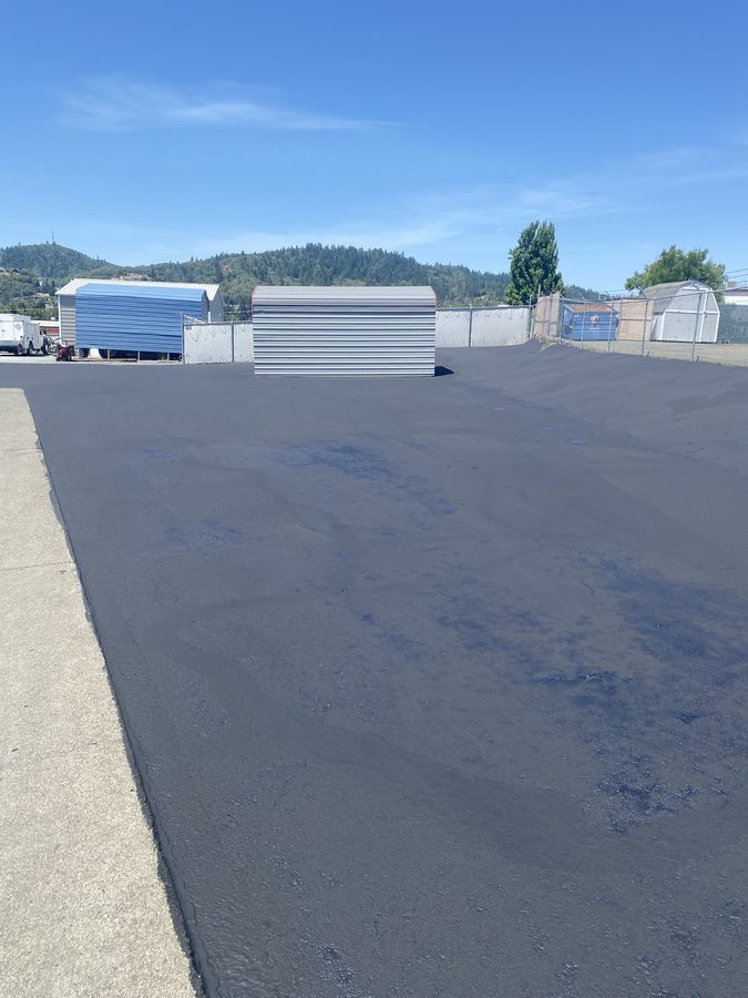 Large commercial parking lot freshly sealcoated across the Caveman Towing yard in Grants Pass, Oregon