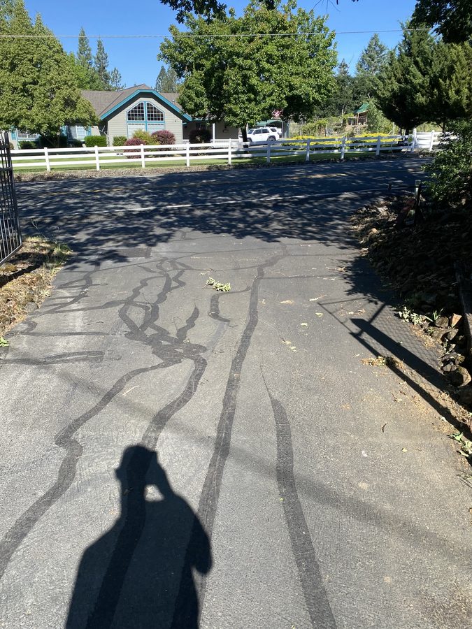 Gray, cracked driveway with rubberized crack filler applied before sealcoating on Soldier Creek Road in Grants Pass, Oregon