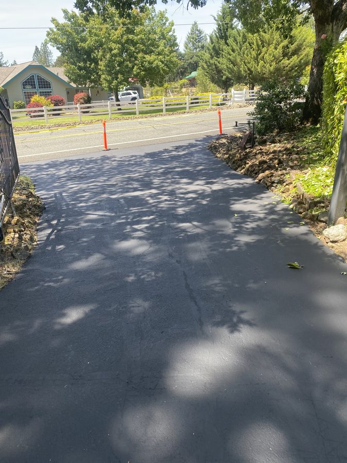 Long residential driveway freshly sealcoated along a white picket fence on Soldier Creek Road in Grants Pass, Oregon