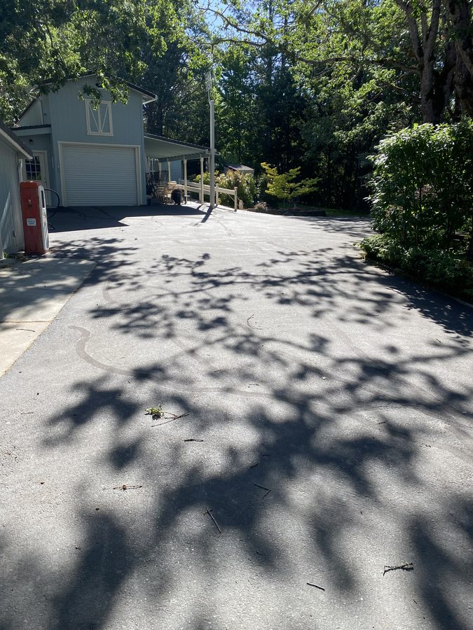 Sun-faded, weathered asphalt driveway with surface cracking before sealcoating on Soldier Creek Road in Grants Pass, Oregon