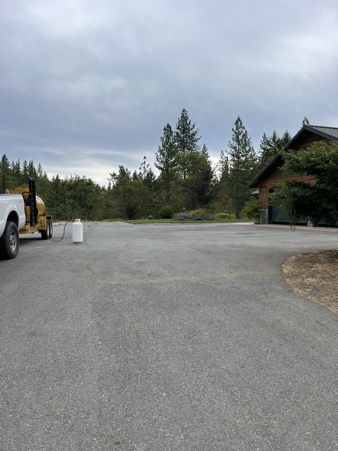 Residential driveway sealcoating in progress with the sealcoat rig parked alongside on Seclusion Loop in Grants Pass, Oregon