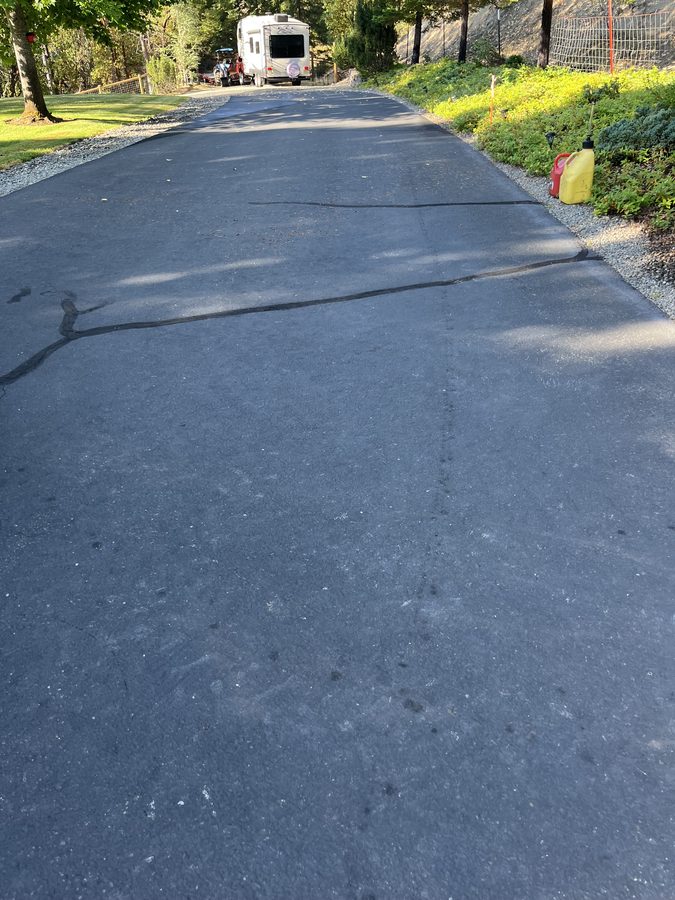 Long rubberized crack filler line sealed across a wide freshly sealcoated asphalt pad on Seclusion Loop in Grants Pass, Oregon