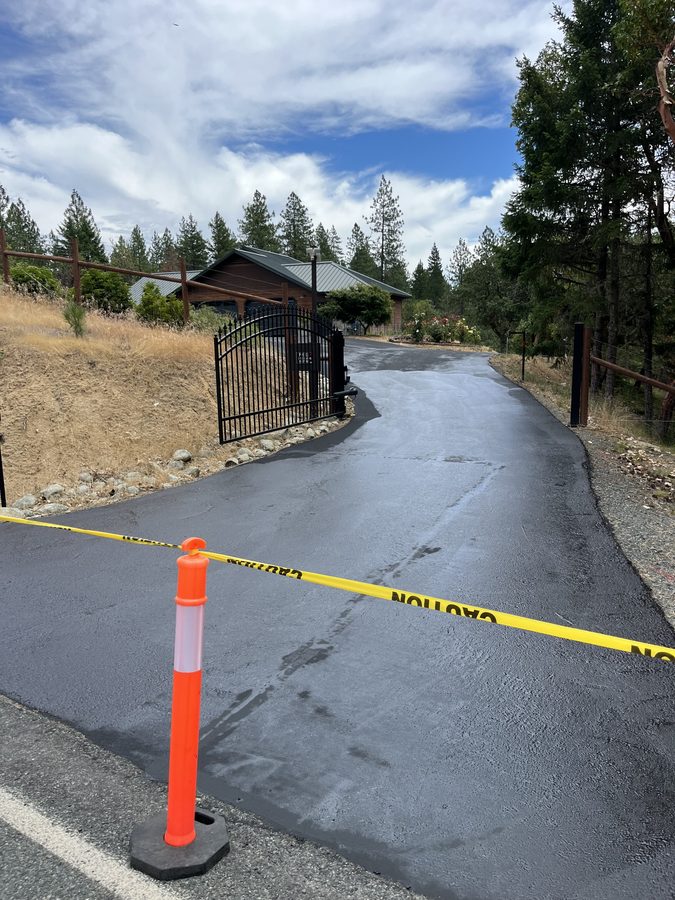 Freshly sealcoated driveway blocked off with yellow caution tape and an orange cone to cure on Seclusion Loop in Grants Pass, Oregon