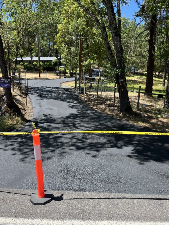 Freshly applied driveway sealcoat taped off with a cone and caution tape to cure on Lower River Road in Grants Pass, Oregon