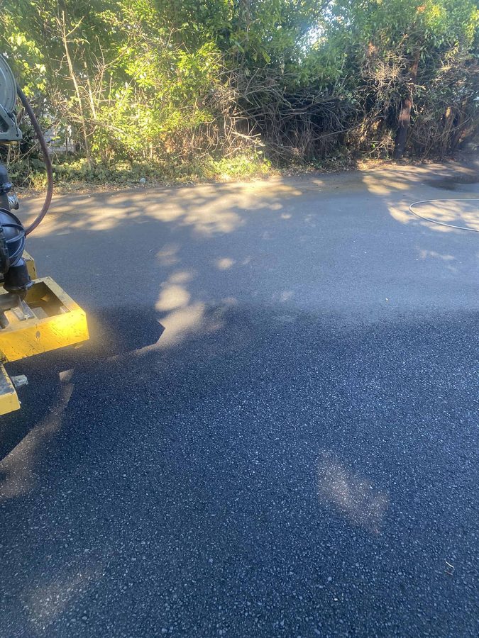 Fresh black driveway sealcoat cut in clean along the landscaping edge with the sealcoat rig alongside on Hazel Street in Central Point, Oregon