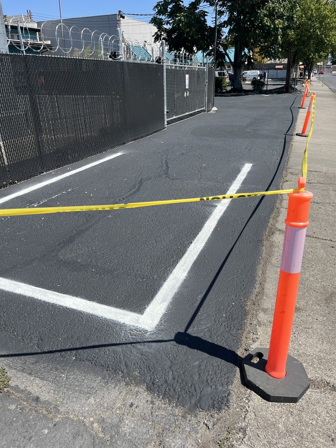 Fresh black sealcoat with newly painted white parking lines coned and caution-taped off to cure on Market Street in Medford, Oregon