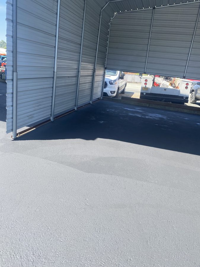 Fresh black sealcoat laid against the building edge in the Caveman Towing yard in Grants Pass, Oregon
