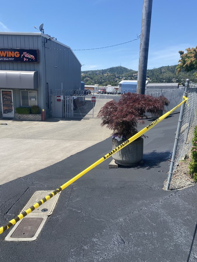 Deep-black freshly sealcoated asphalt beside the Caveman Towing entrance on 2100 NW Vine St in Grants Pass, Oregon