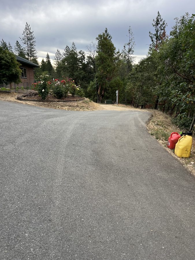 Freshly sealcoated residential asphalt driveway with a deep-black finish under a blue sky on Seclusion Loop in Grants Pass, Oregon