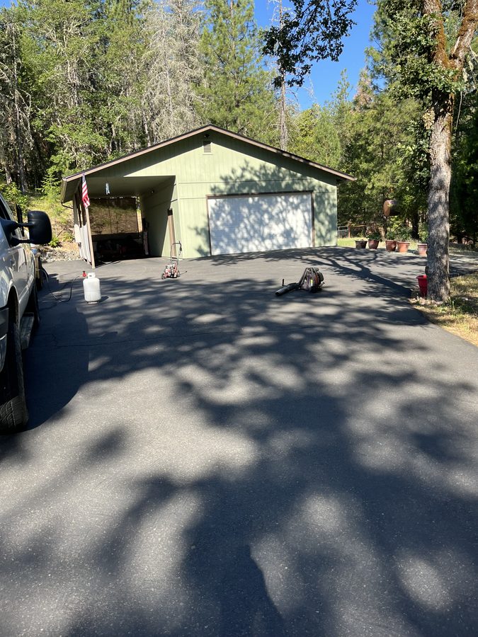 Freshly sealcoated asphalt driveway with a deep-black finish in front of a home on Lower River Road in Grants Pass, Oregon