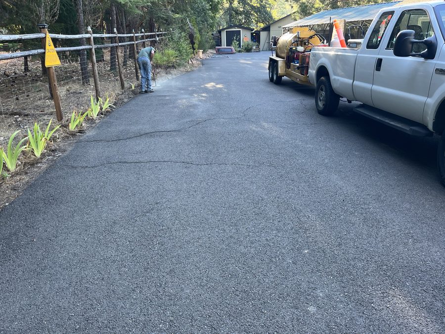 Neill Sealcoating truck with a hot-pour crack-filling kettle and traffic cones set up on a residential asphalt driveway on Hidden Valley Road in Grants Pass, Oregon