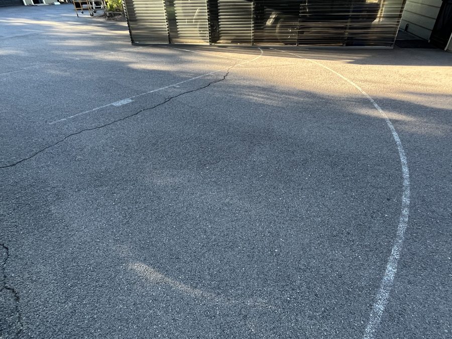 Close-up of oxidized gray asphalt with spreading surface cracks outside a garage before crack filling and sealcoating on Hidden Valley Road in Grants Pass, Oregon
