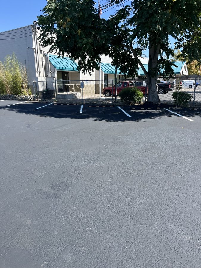 Freshly sealcoated commercial parking lot with new white stall striping and wheel stops on Market Street in Medford, Oregon
