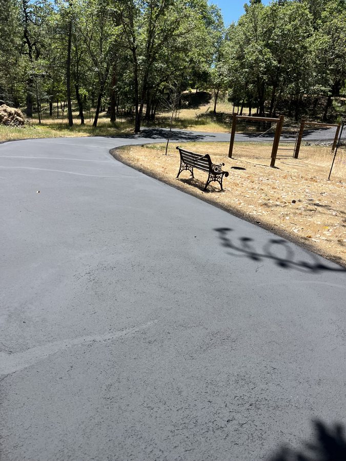 Smooth freshly sealcoated residential driveway beside a garden bench on Lower River Road in Grants Pass, Oregon