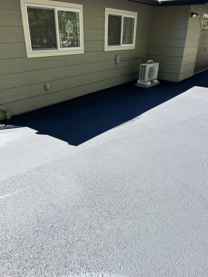 Fresh asphalt sealcoat cut in cleanly along the edge of a home's siding and foundation on Hidden Valley Road in Grants Pass, Oregon