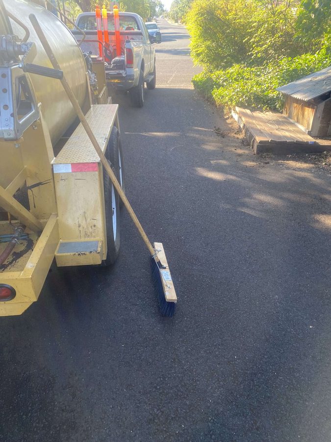 Push broom resting on a freshly sealcoated driveway beside the Neill Sealcoating rig and truck on Hazel Street in Central Point, Oregon