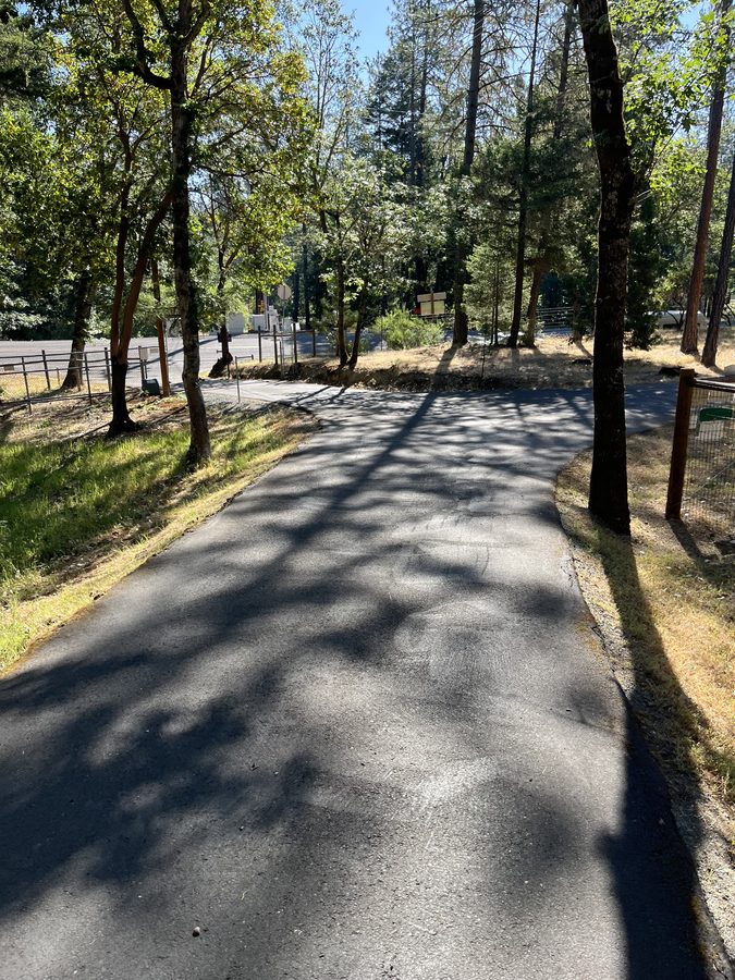 Sealcoated asphalt driveway running clean along a fence line and tree row on Lower River Road in Grants Pass, Oregon