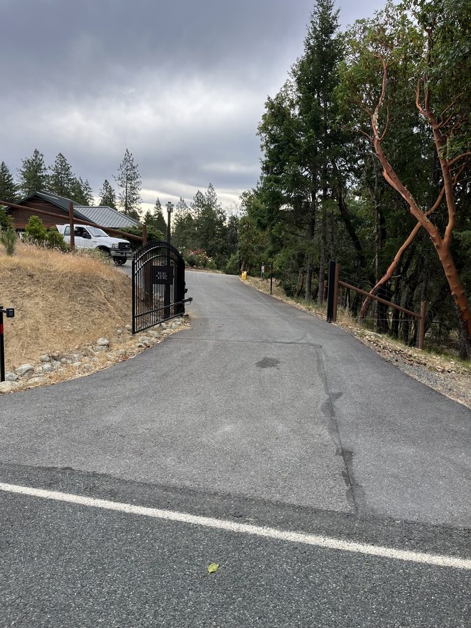 Freshly sealcoated private asphalt lane curving between a gravel shoulder and trees on Seclusion Loop in Grants Pass, Oregon