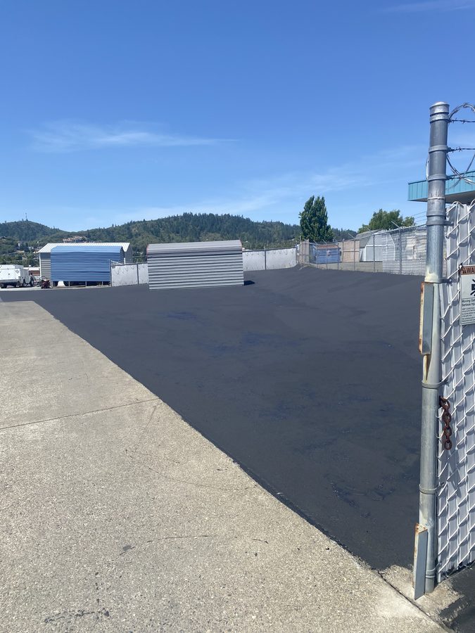 Freshly sealcoated commercial storage yard behind a security gate at Caveman Towing in Grants Pass, Oregon