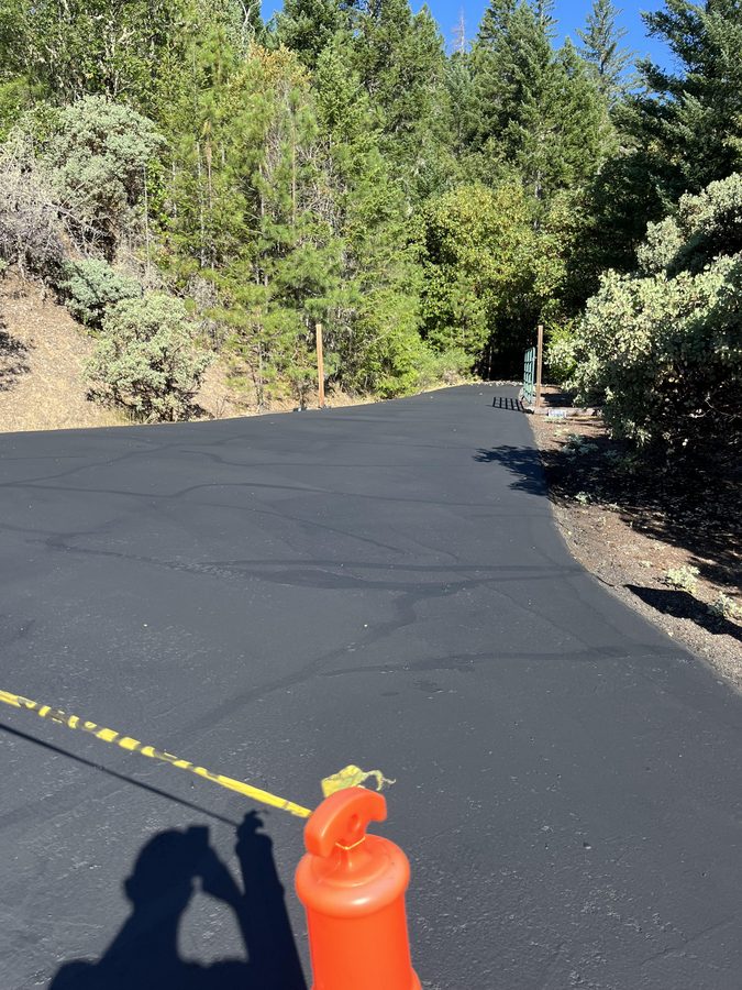 Freshly sealcoated hillside driveway approach blocked off with an orange cone and caution tape to cure on Seclusion Loop in Grants Pass, Oregon