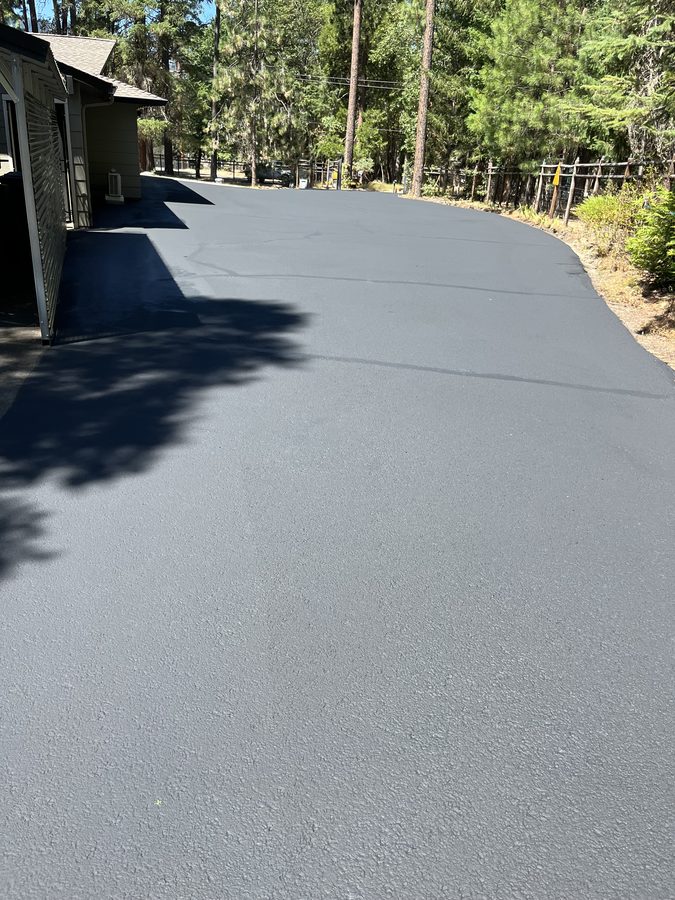 Smooth freshly sealcoated asphalt driveway curving past a covered deck and pine trees on Hidden Valley Road in Grants Pass, Oregon