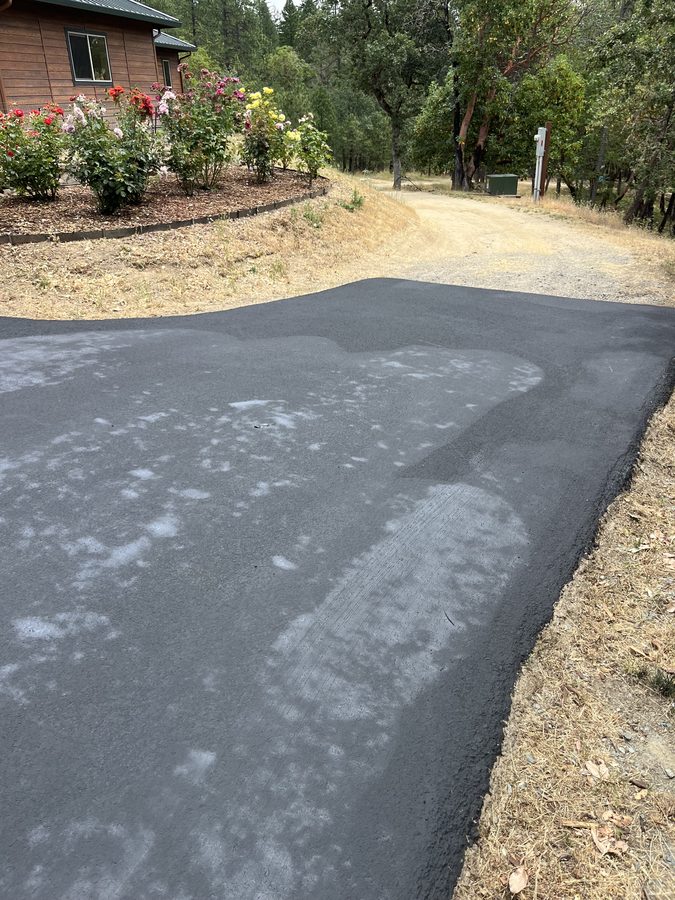 Freshly sealcoated driveway curving past a flower garden and cabin on Seclusion Loop in Grants Pass, Oregon