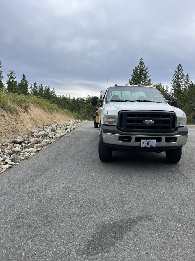 Smooth, freshly sealcoated asphalt driveway lined with trees and fencing on Seclusion Loop in Grants Pass, Oregon