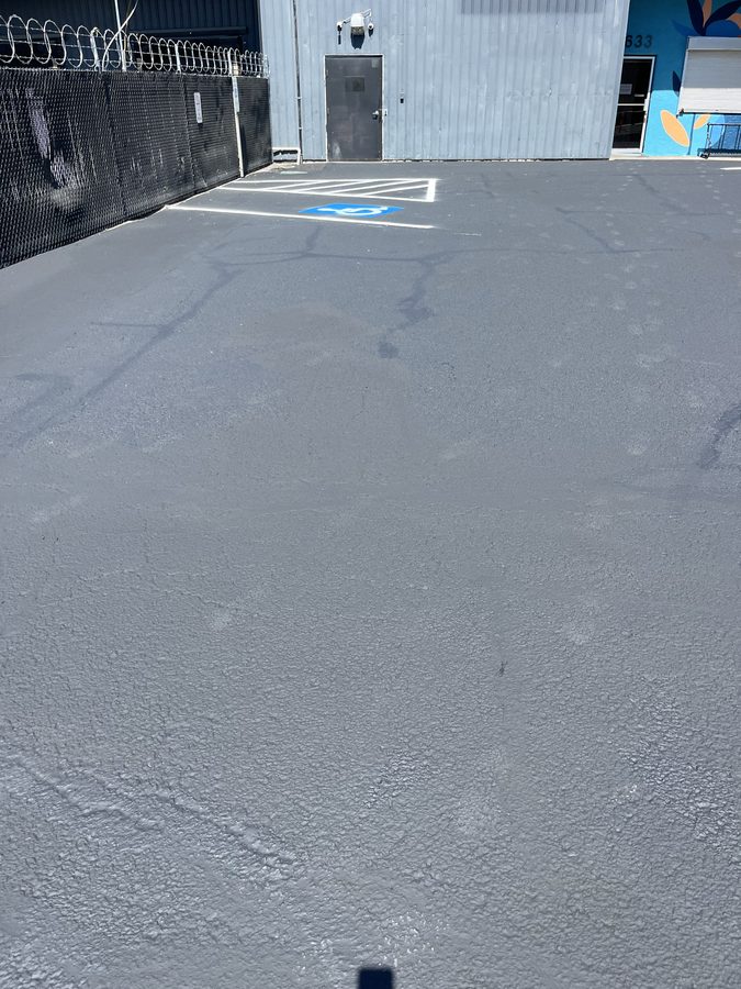 Freshly sealcoated parking area with repainted ADA access-aisle hatching and accessible-parking signage on Market Street in Medford, Oregon