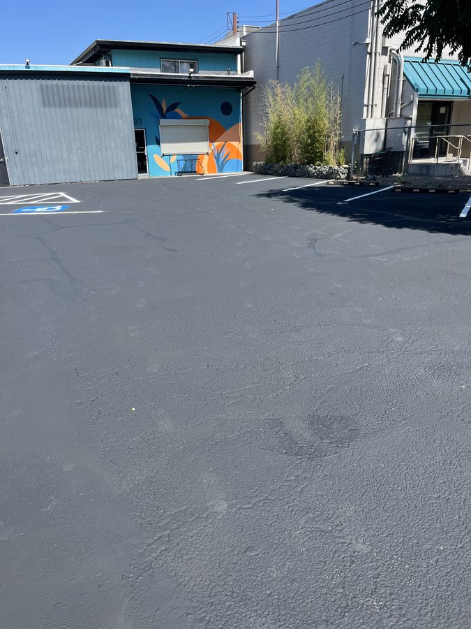 Wide view of a smooth, freshly sealcoated commercial parking lot surface with new white striping on Market Street in Medford, Oregon