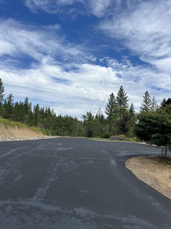 Long tree-lined asphalt lane freshly sealcoated and curving through the property under a dramatic sky on Seclusion Loop in Grants Pass, Oregon