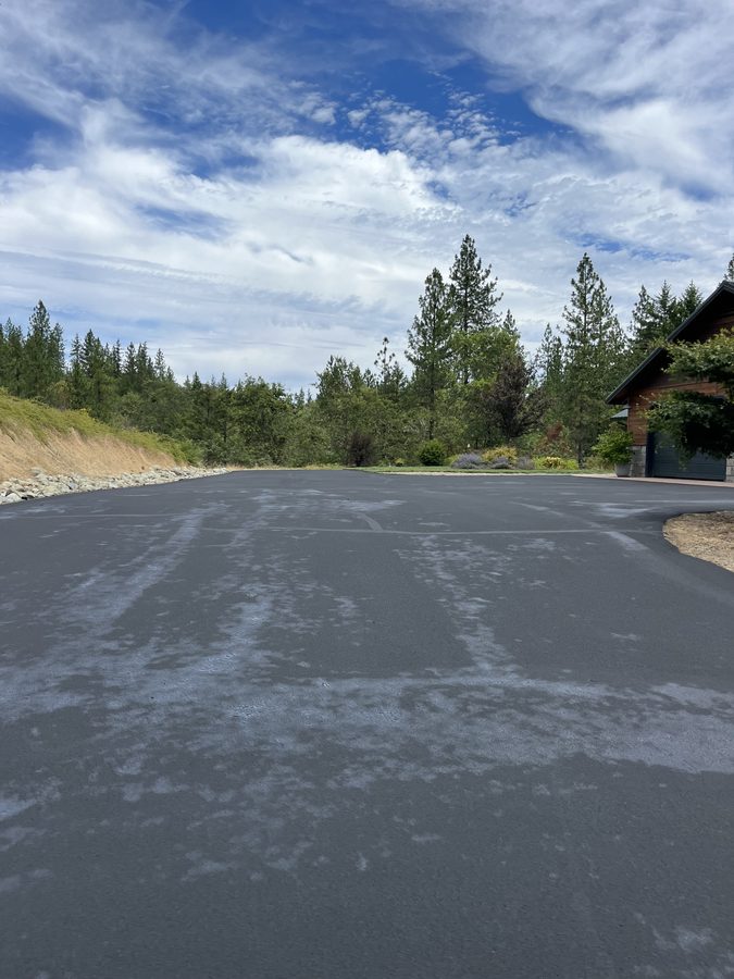 Wide freshly sealcoated asphalt driveway curing under a blue sky beside a home on Seclusion Loop in Grants Pass, Oregon
